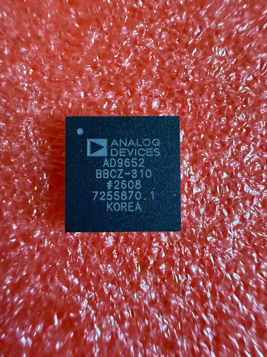 A single black rectangular electronic chip with white printed text, including the brand 'ANALOG DEVICES' and model 'AD5652', placed on a textured orange-red background.